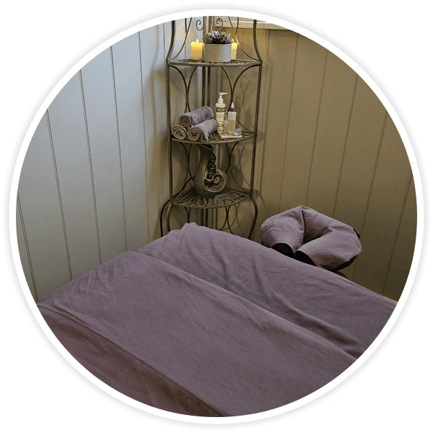 A bed with purple sheets and pillows in front of a corner shelf.